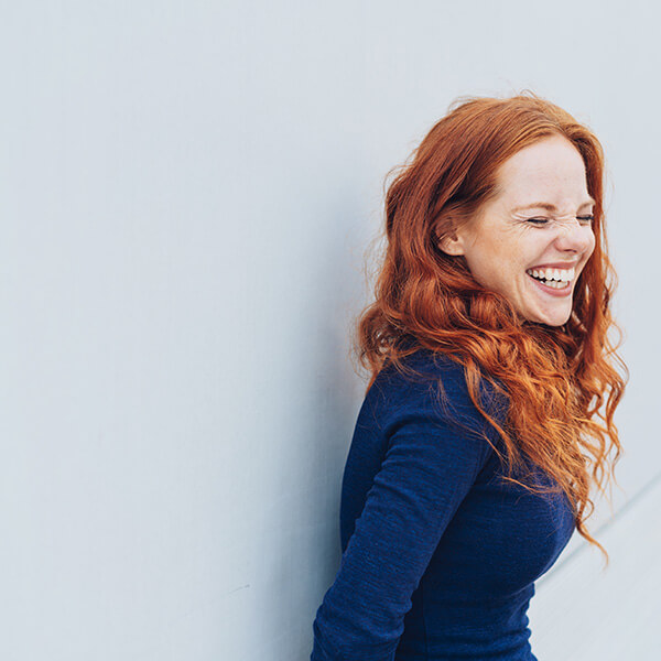 woman with red hair leans against a wall, laughing